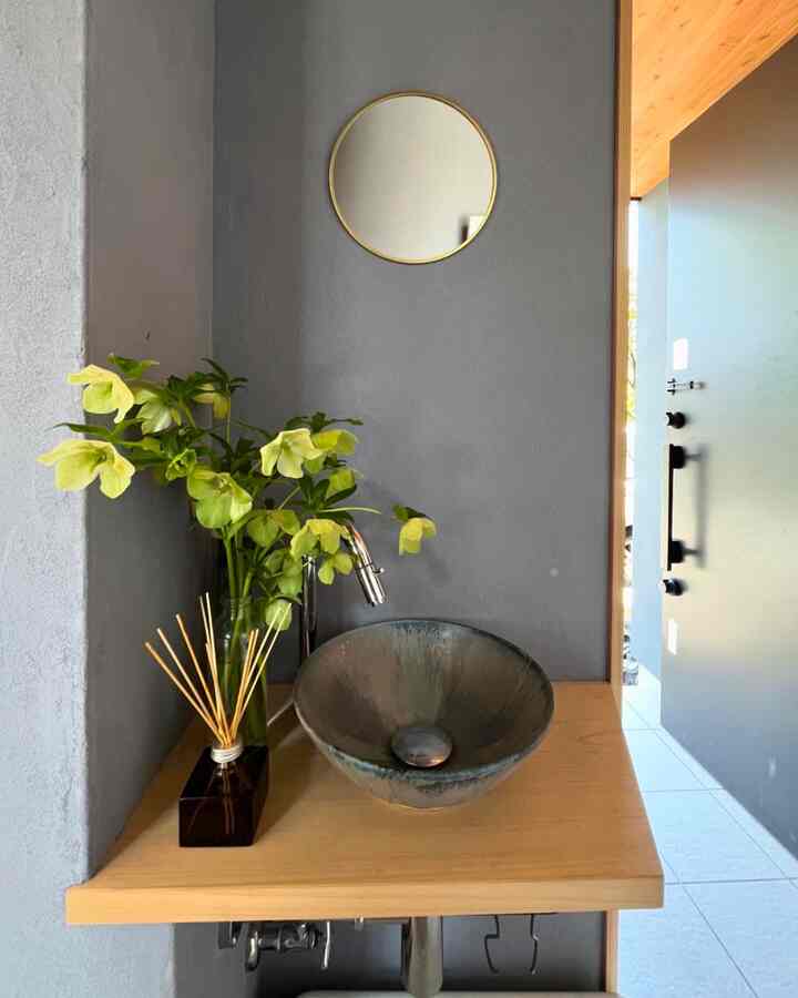 Entrance area with gray wall and wood-toned shelf featuring a round mirror and a hand wash basin, creating a simple, natural atmosphere