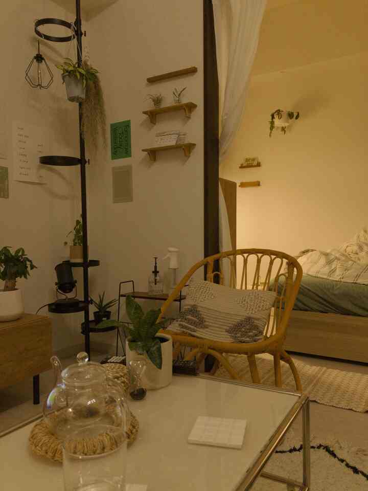 Warm beige-toned studio apartment living-bedroom featuring rattan chair and glass coffee table with cozy atmosphere