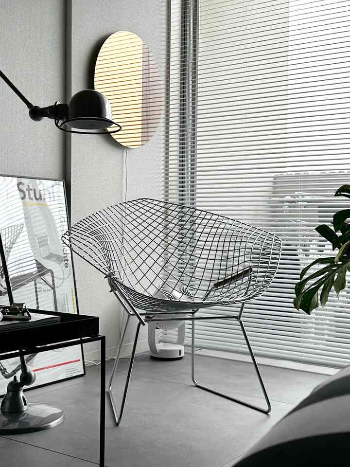 グレーの床と壁が包む、モダンでインダストリアルな雰囲気のベランダ、ワイヤーチェアと黒いフロアランプが配置されたミニマルな空間