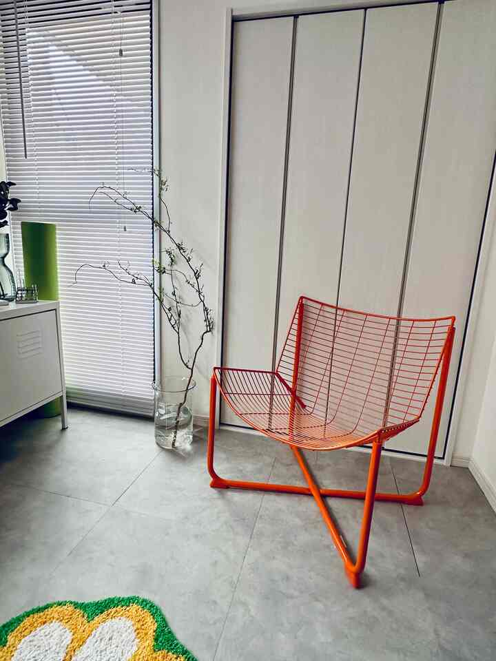 Small space in white and green tones featuring an orange wireframe armchair and blinds, styled in a clean modern interior