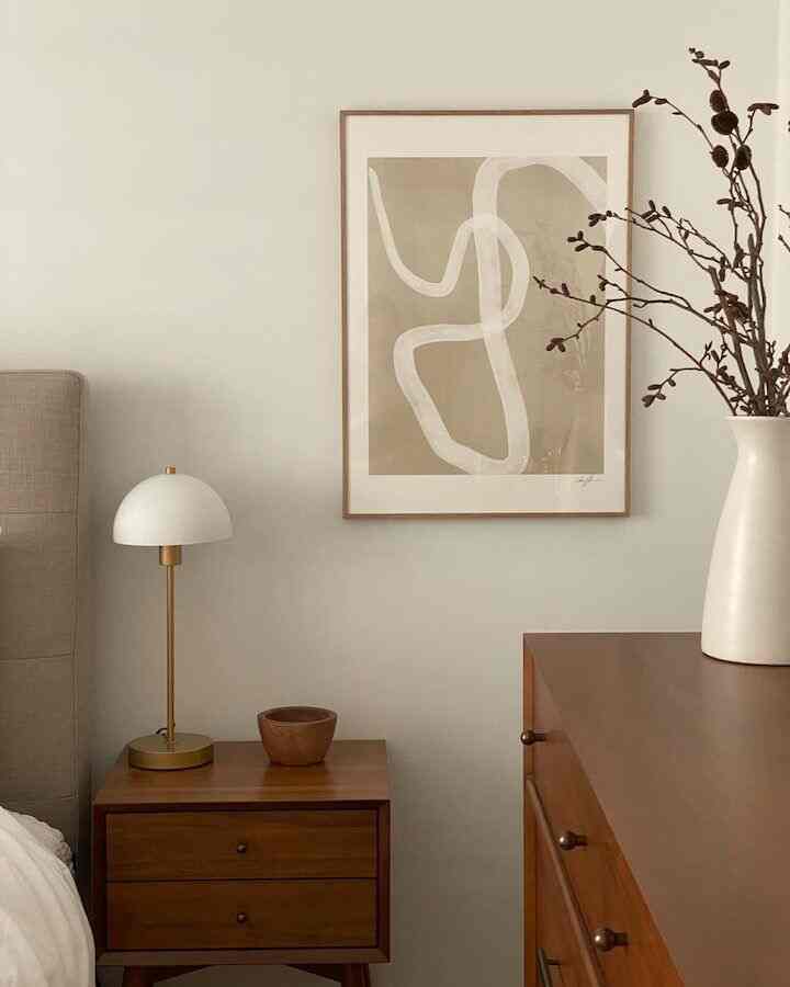 Wood tone bedroom featuring a nightstand, dresser, and gold-accented table lamp with a calm atmosphere