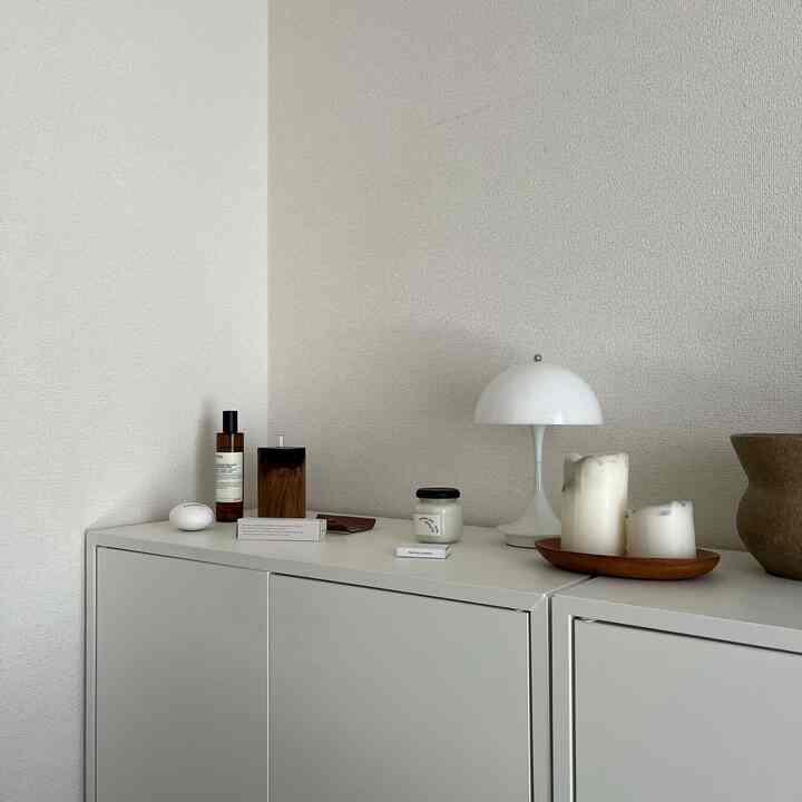 白とナチュラルカラーのワンルーム、シンプルなチェストの上にテーブルランプやキャンドルなどのオブジェが配置された雰囲気のあるインテリア