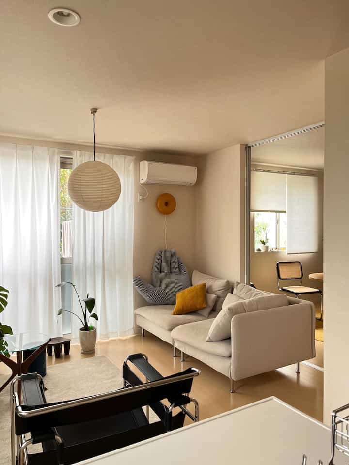 Beige and white toned living room featuring a beige sofa, black armchair, round pendant light with modern natural ambiance