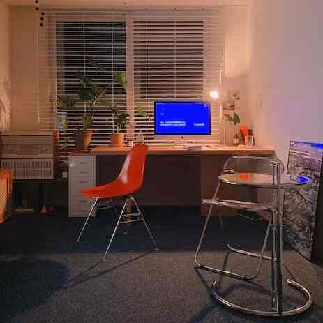 Cozy home office for single household featuring blue carpet, brown wooden desk, red chair, and plants with relaxed atmosphere