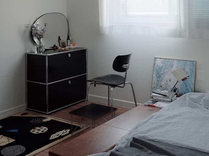 A compact bedroom in white and black tones featuring a modern vanity and sleek chair with a clean, chic ambiance