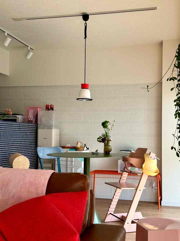 Natural modern dining room with white walls, brown leather sofa, green dining table, and pink baby chair creating a warm atmosphere