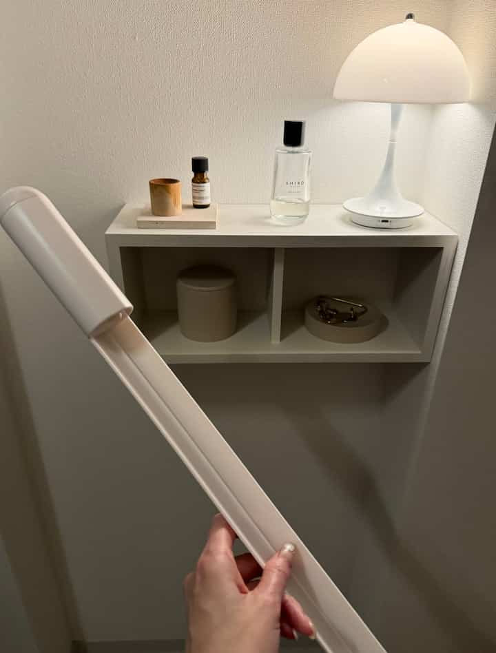 White-toned entrance area featuring a small shelf with a lamp, bottles, and minimal decor in a tidy setting