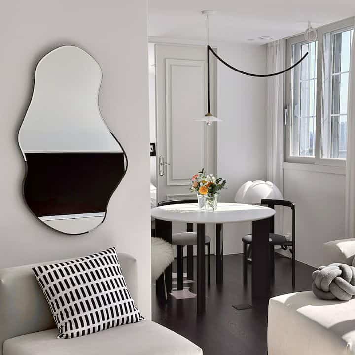 Monotone living-dining room featuring a white round table, black chairs, and an abstract shaped mirror in a sleek interior