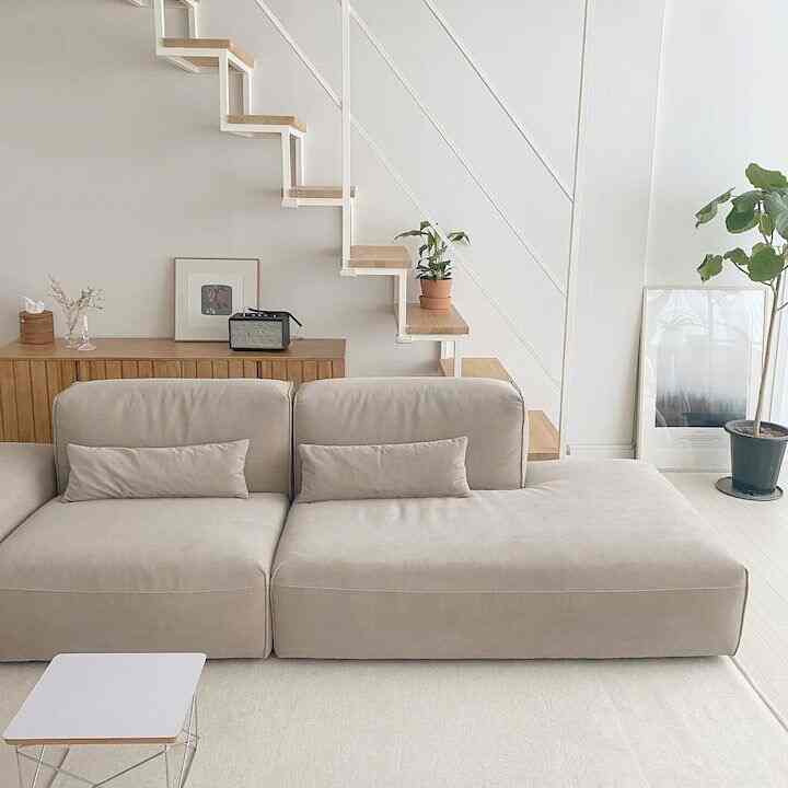 Bright white walled living room with natural wood stairs and under-stair storage, featuring a beige sofa and minimal decor