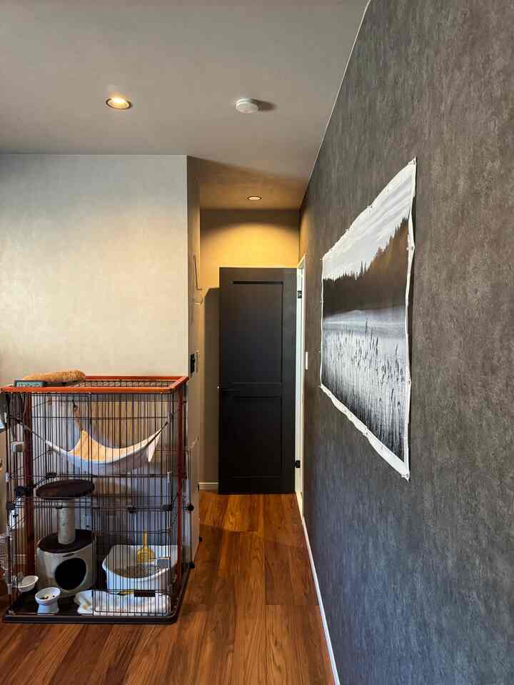グレーの壁と木目調の床がある廊下の空間、大きな犬用ケージが配置され、居心地の良く実用的な雰囲気のインテリア