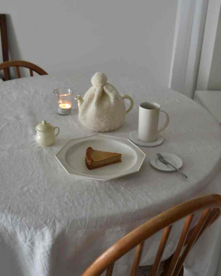 白いテーブルクロスを敷いたダイニングテーブルの上にティーポット、カップ、ケーキの一切れ、灯されたキャンドルが置かれた印象的な二人暮らしのおうちカフェ