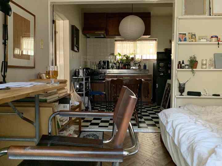 ホワイトとブラウンの色調のワンルームキッチンと寝室が配置された、自然な雰囲気の落ち着いた空間