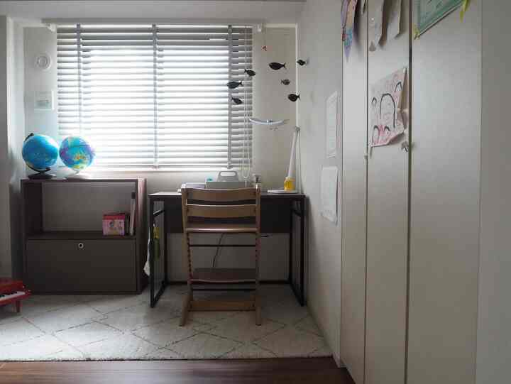 Bright white and beige-toned kids' room featuring wooden desk and chair with children's drawings on the wall, creating a natural study area