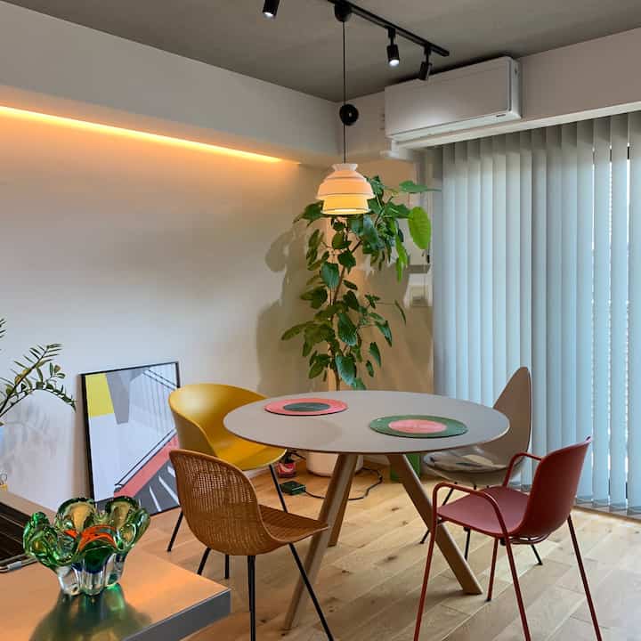 ナチュラルな色調のダイニング、円形のダイニングテーブルに多彩な色の椅子が配置された雰囲気のある空間