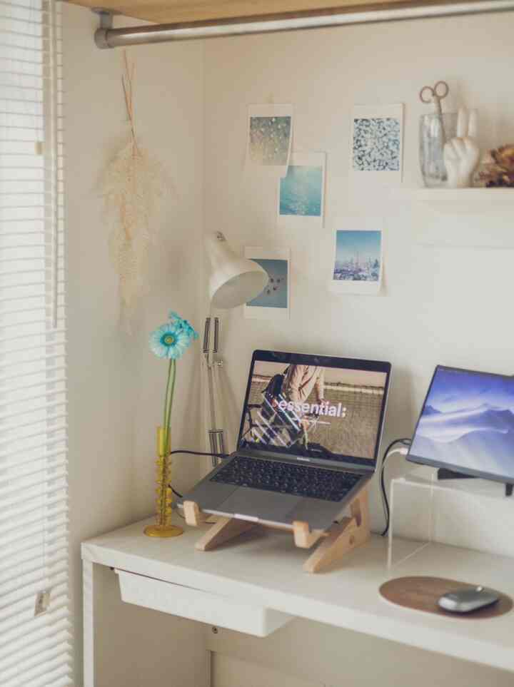 白と黄色のトーンのワークスペース、木製のノートパソコンスタンドと花瓶が配置されたシンプルで清潔感のあるデスクインテリア