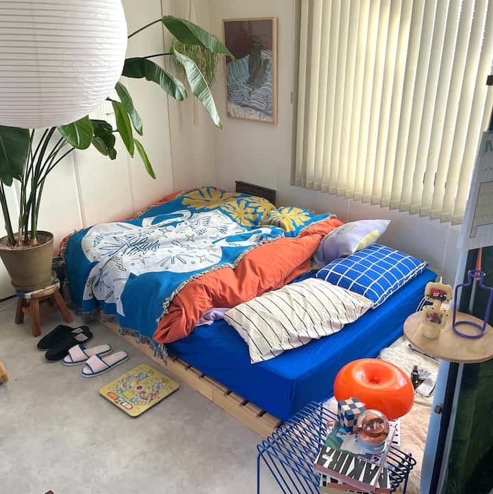A compact bedroom with natural wood tones and blue and orange bedding for a single occupant