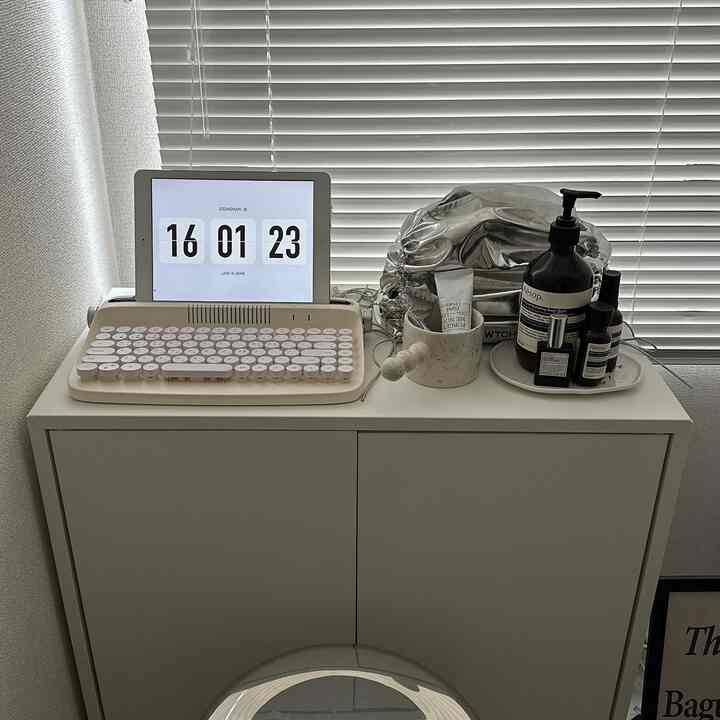 A white-toned compact home office space featuring a tidy cabinet with a retro keyboard and digital clock, creating a simple interior
