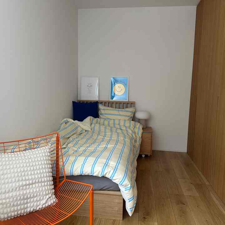 白い壁と木目調の床が特徴の8畳の子供部屋、ストライプ布団とナイトテーブルを配したモダンで落ち着いた空間