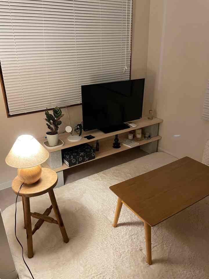 ベージュ色の壁と木目調家具が調和する暖かい雰囲気の小さな寝室、テーブルランプが温かい光を届ける空間