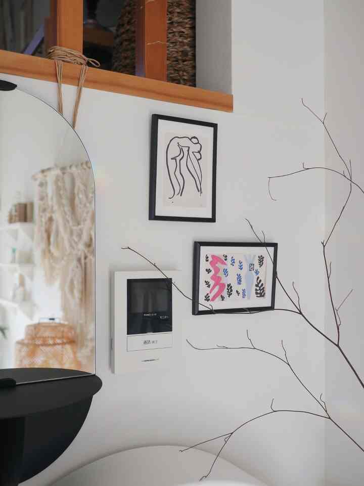 白い壁に黒い額縁が掛かった小さな空間、半円形の鏡とドライプラントが調和するシンプルなインテリア