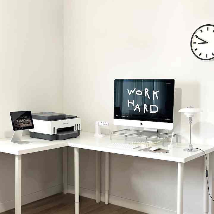 White and monotone home office featuring an L-shaped white desk with a computer, printer, and table lamp creating a minimal workspace