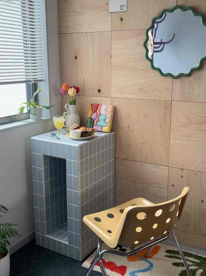 Cafe style corner with wood tone paneled wall and white walls, pastel blue tiled dining table and yellow dining chair by the window