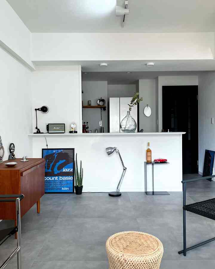 白とナチュラルトーンのシンプルなリビング、黒い金属製の椅子とラタンのスツールが配置された清潔感のある空間