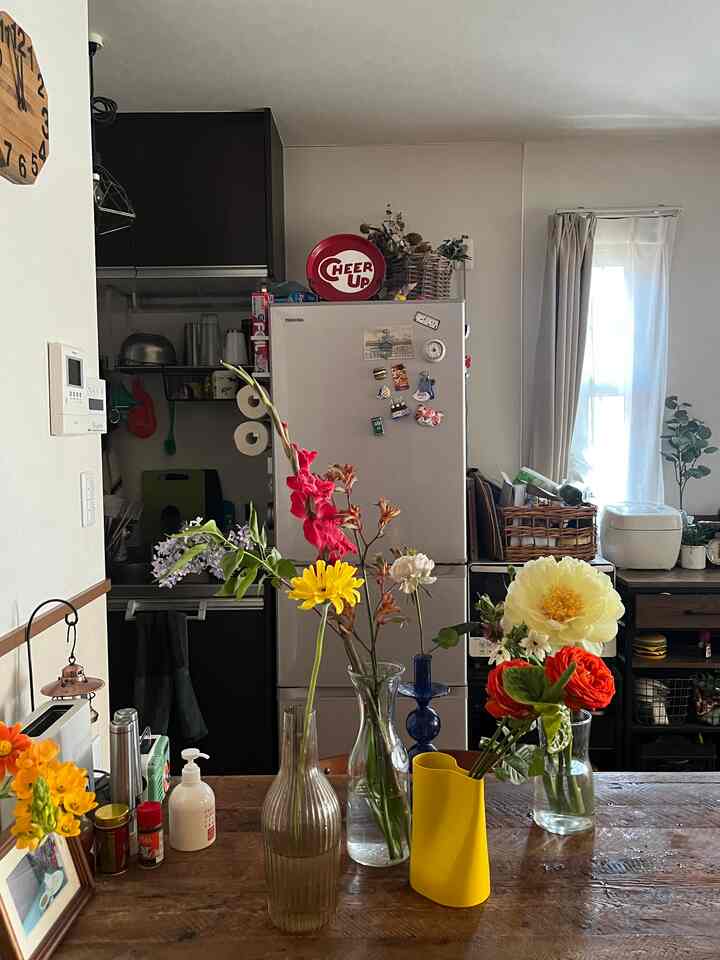 Natural small kitchen space with white walls and wood tone dining table, featuring colorful flower vases with fresh flowers