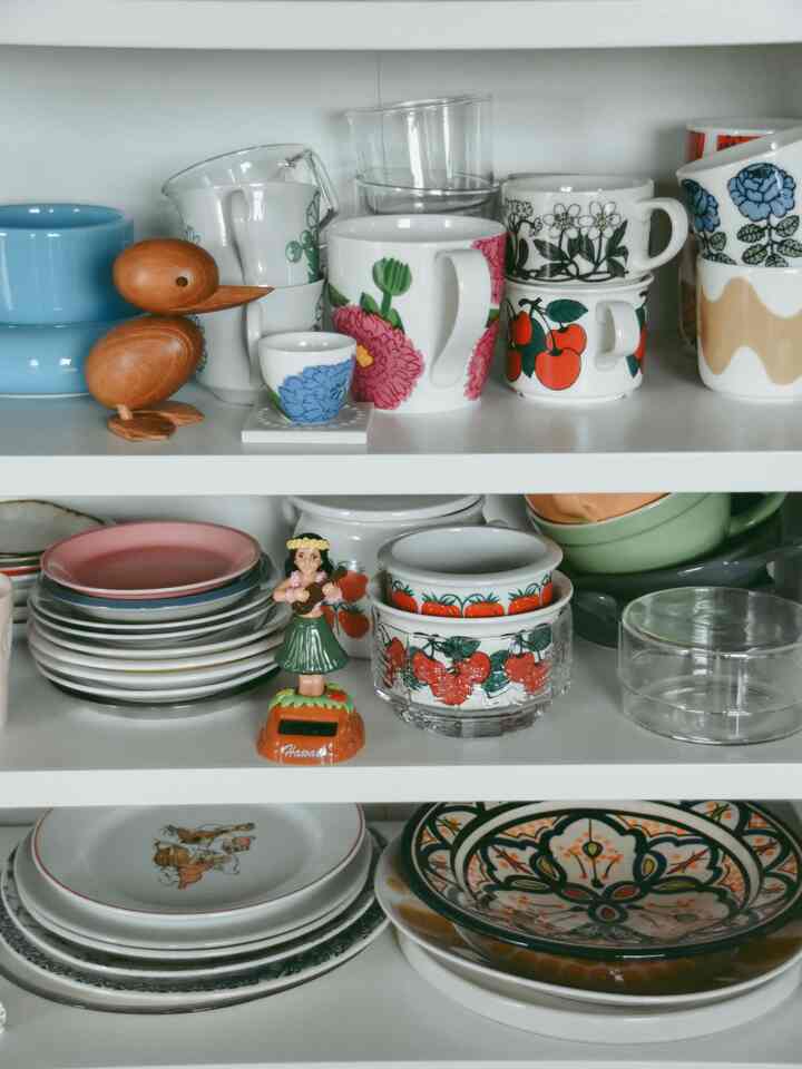 White shelves in kitchen storing colorful floral tableware and wooden decorative objets, creating an organized and natural atmosphere