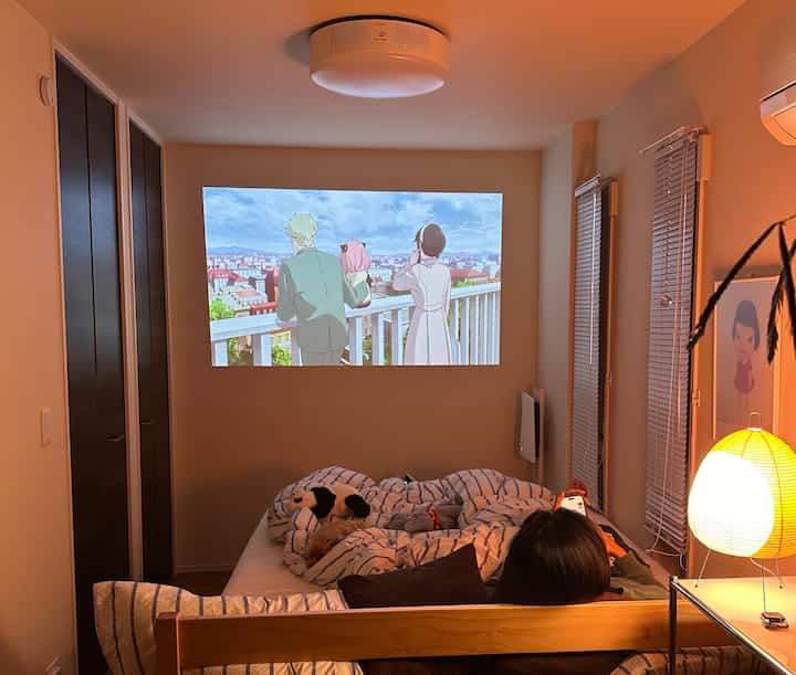 温かみのあるライトブラウンのナチュラルな寝室、無印良品の木製ベッドとイサムノグチ風スタンドランプが配置された雰囲気のあるホームシネマ空間