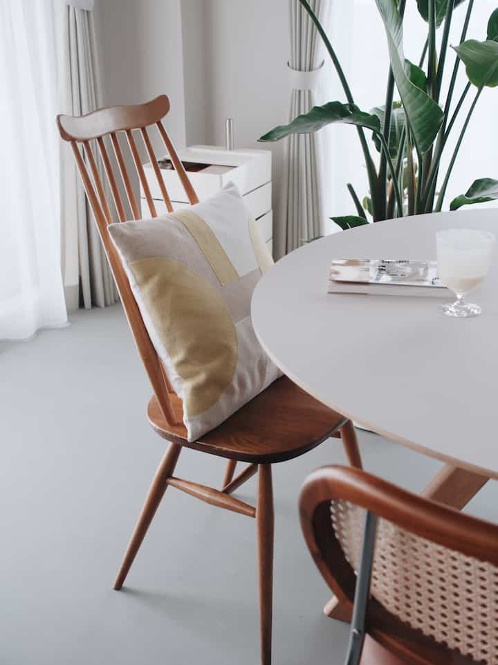柔らかな白と茶色のナチュラルトーンのダイニング、アーコールの木製チェアとクッション、大きな観葉植物が配置された落ち着いた空間