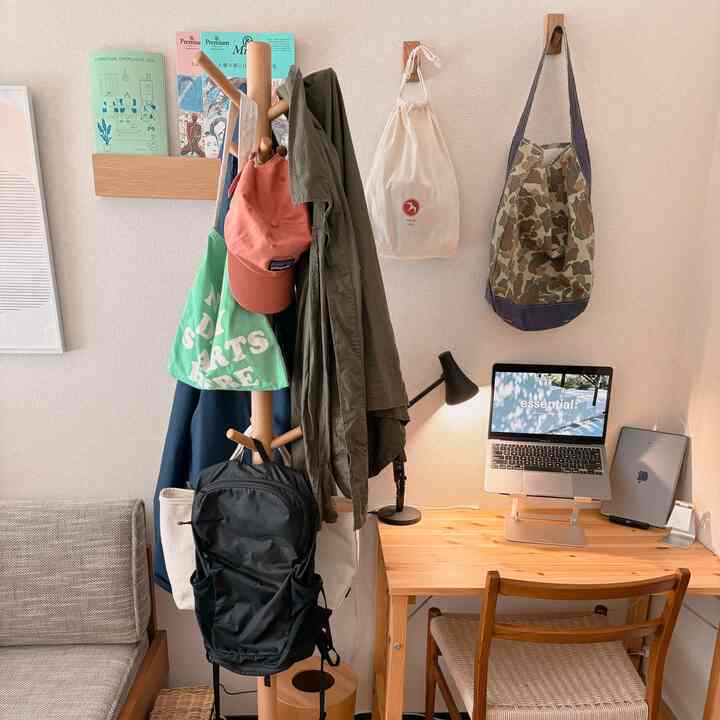 ベージュの壁と木目調家具が配置された一人暮らしのホームオフィススペース、デスク上のノートパソコンと吊るされた服のあるハンガーラックで落ち着いた雰囲気