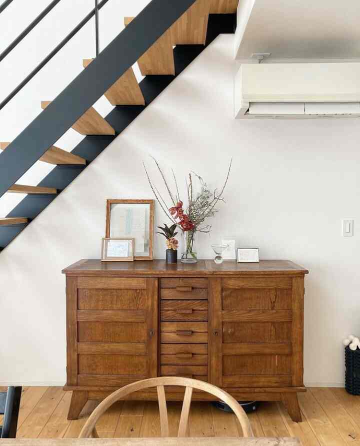 Minimal entrance space under stairs featuring white walls and wooden tone cabinet with decorative items