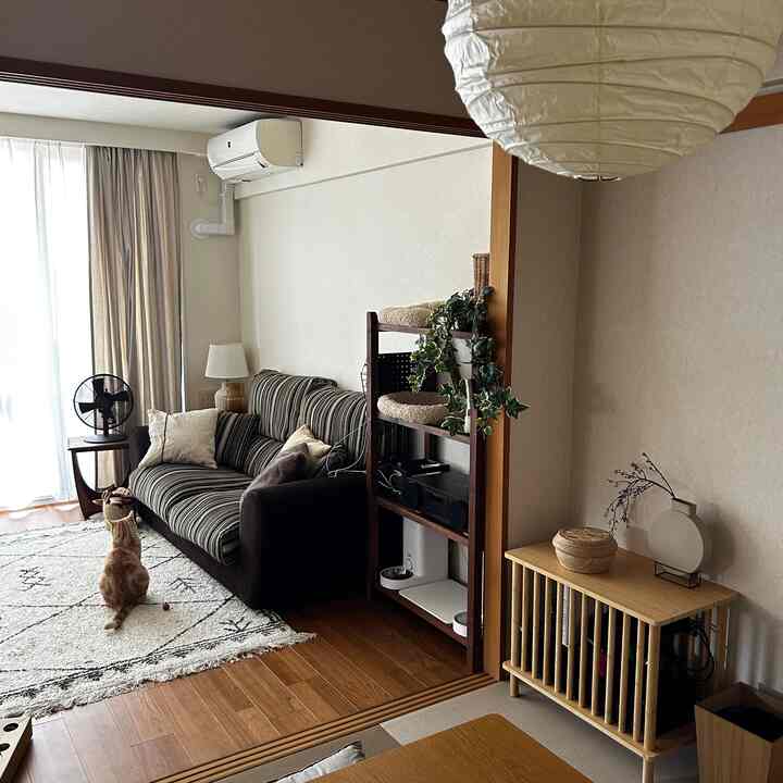 Wood-tone floored living room with white walls featuring a striped sofa, cat tower, and a sitting orange cat creating cozy atmosphere