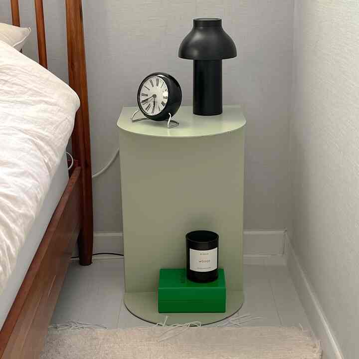 A bedroom with white background and light green nightstand, featuring a black table lamp and alarm clock, showcasing a neat minimal space