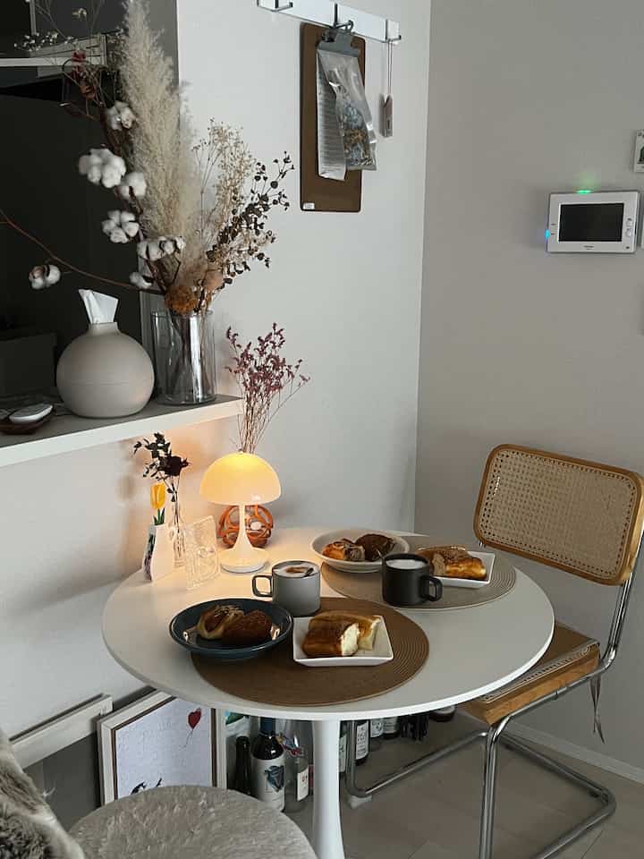 ナチュラルカラーのワンルームキッチンとダイニング空間、ラタンチェアとテーブルランプが配置されたシンプルなインテリア