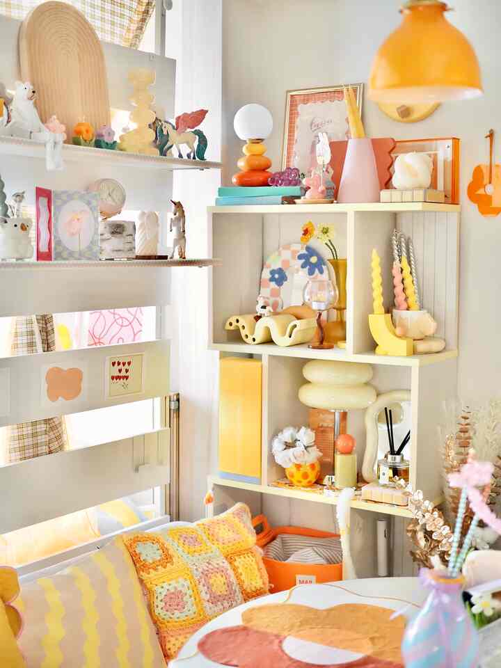 A warm living room corner in orange and yellow tones featuring colorful cushions, shelves, and various decorative items