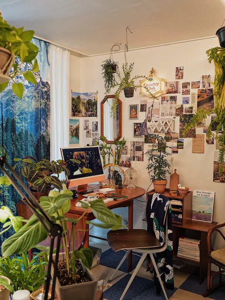 A cozy home office space featuring brown wood furniture and green plants, with wall decorated by photos and posters