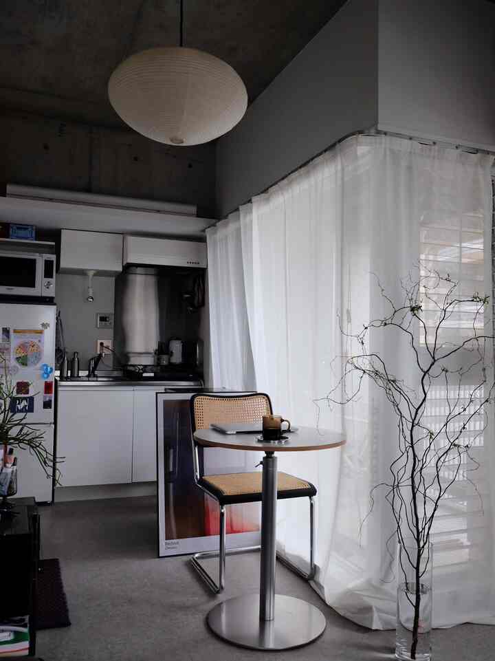 White and gray toned studio apartment featuring a single round table, pendant light, and natural material furniture in a minimal setting