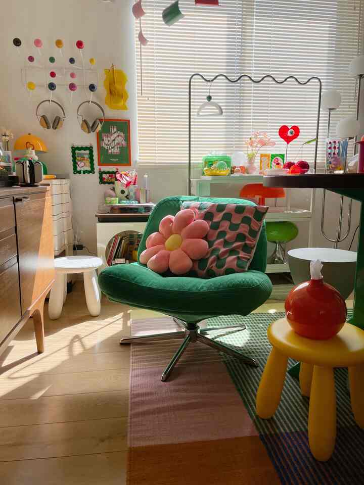 カラフルな小さな部屋に、中央には花の形のクッションと幾何学模様のクッションが置かれた緑の回転式アームチェアが配置された雰囲気のあるレトロなインテリア