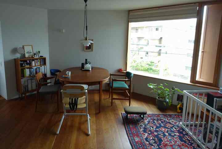 ナチュラルな木目調と大きな窓がある明るいリビング、ダイニングテーブルと子供用安全フェンスが配置された空間