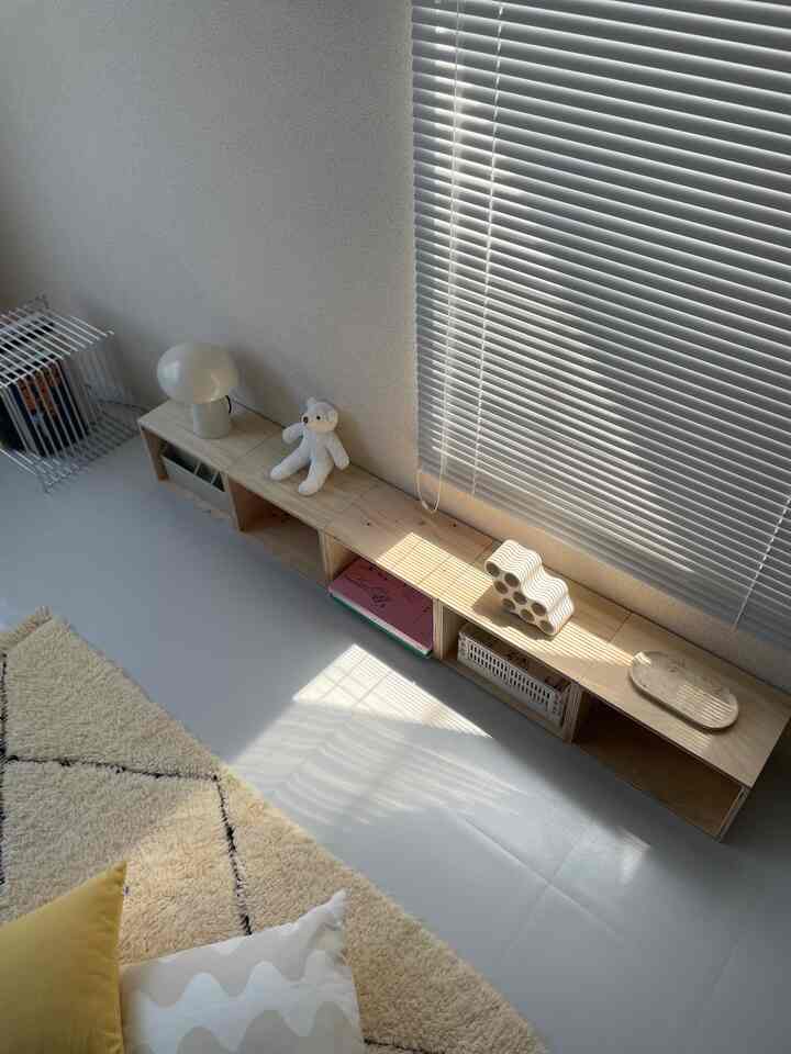 White-toned living room featuring a natural wood low storage shelf with warm sunlight and a simple, cozy atmosphere