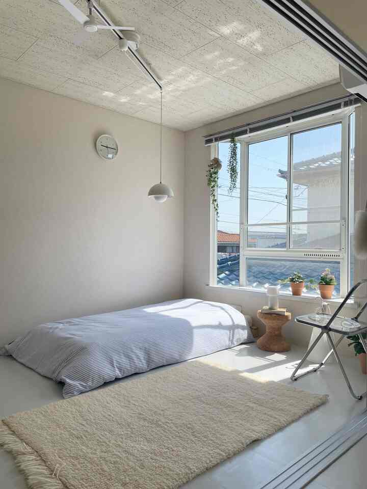 白と木目調の6畳寝室、床にマットレスを敷き、コルクスツールと植物が配置された自然で落ち着いた雰囲気のインテリア