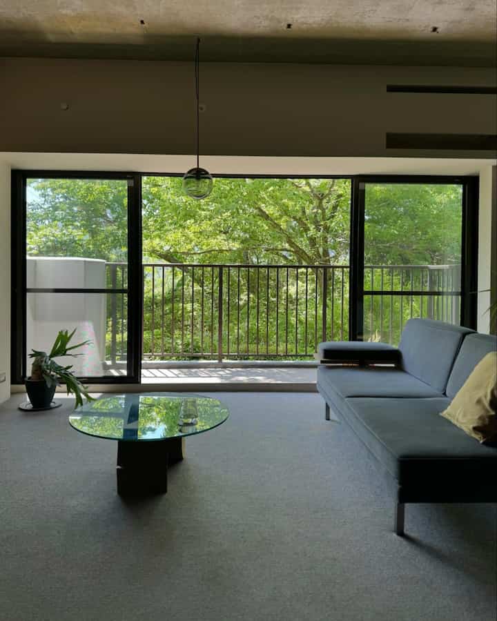 Green-dominant living room with large windows connecting to balcony and nature, featuring modern design
