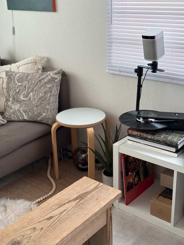 ナチュラルな木目調の一人暮らしリビング、グレーのソファと白の丸テーブル、本棚が配置された落ち着いた雰囲気のインテリア