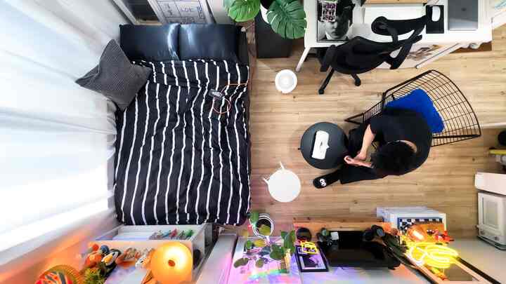 黒いストライプの寝具がある寝室とデスク、オフィスチェアが配置されたコンパクトな一人暮らしのワンルーム、温かみのある空間