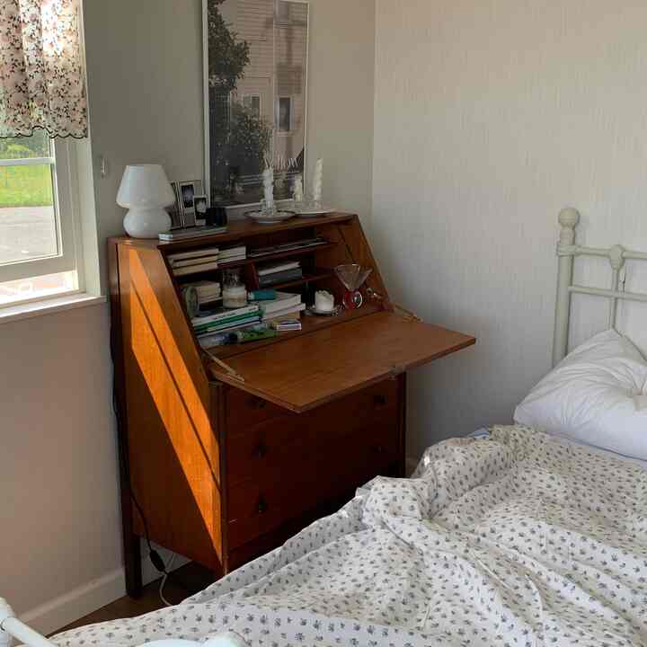A bedroom with white walls and a brown wooden desk, illuminated by soft natural light creating a cozy atmosphere