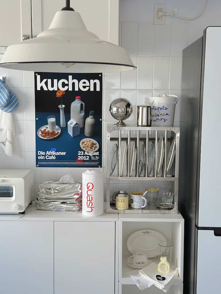 白とステンレスの調和が取れたキッチン、中央にポスターと整頓された食器乾燥ラックが配置されたシンプルな空間