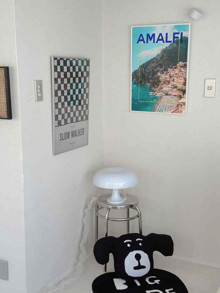 White-toned corner space featuring a stainless round stool, a dog-faced cushion, and wall posters creating a cozy vibe