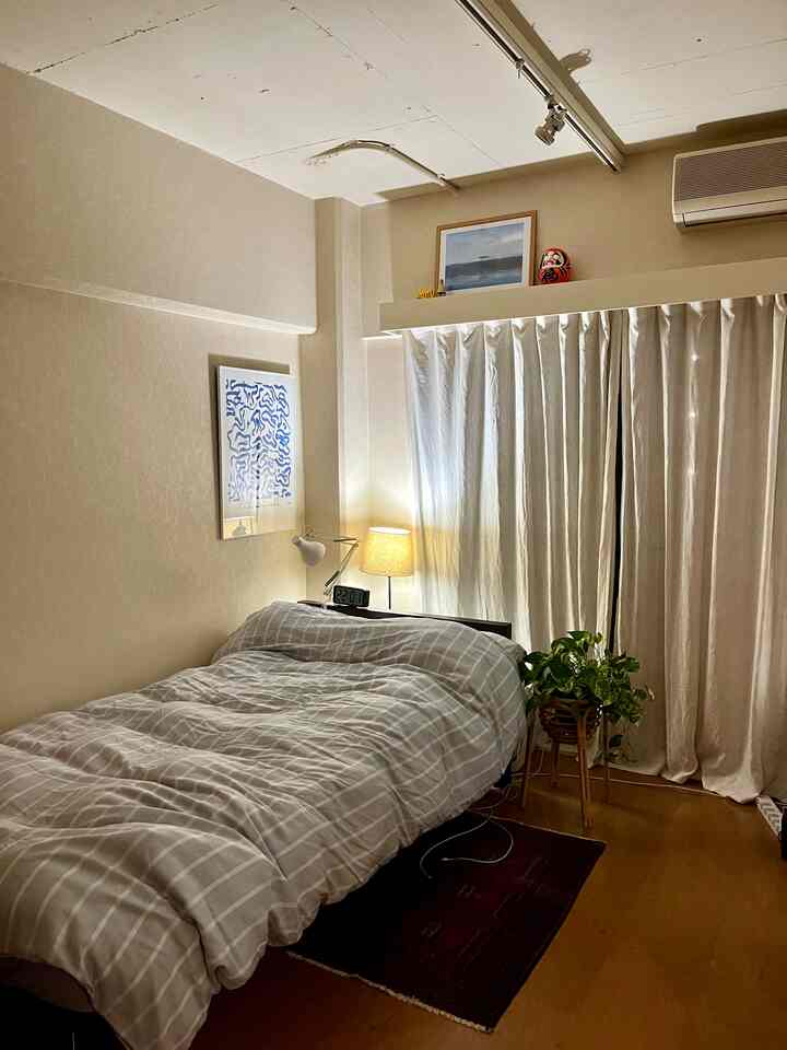 ナチュラルカラーの寝室、ベージュの掛け布団と照明、観葉植物が配置された雰囲気のあるインテリア